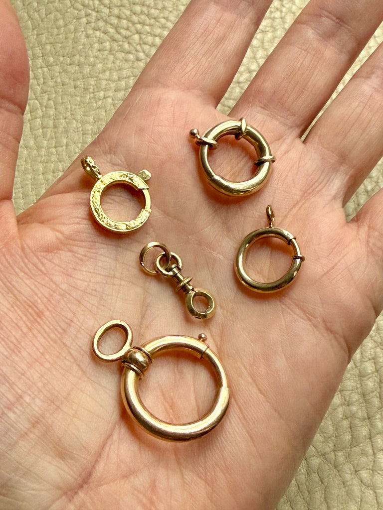 Gold bolt clasps on a hand with a beige background PenelopePenelope.com