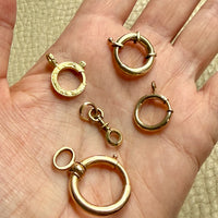 Gold bolt clasps on a hand with a beige background PenelopePenelope.com