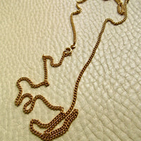 An 18k gold chain necklace with a curb link style, laid out on a textured beige leather surface.