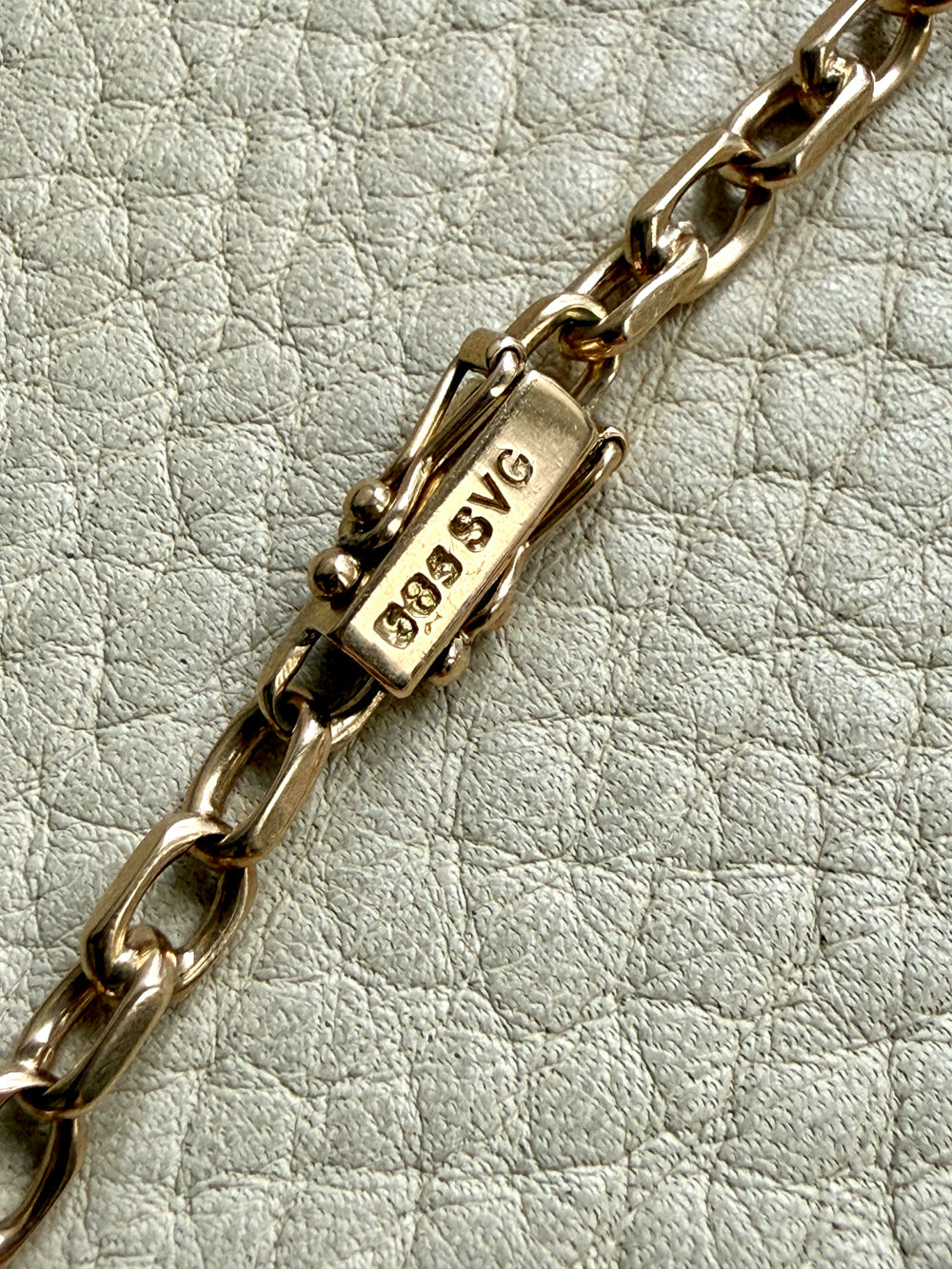 Gold chain bracelet with a clasp on a textured light gray background