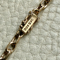Gold chain bracelet with a clasp on a textured light gray background