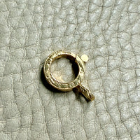 Gold bolt clasp pendant on a textured gray surface