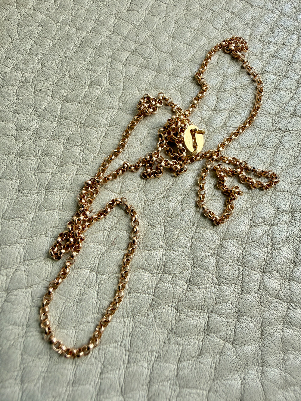 18k Gold rolo link necklace on a textured light green surface