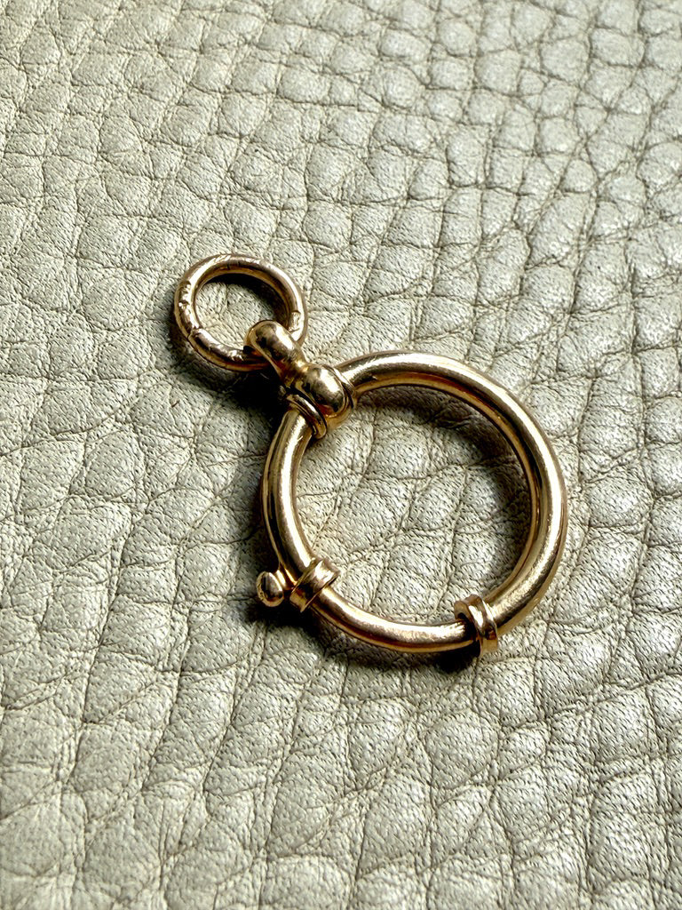 18k Gold antique bolt ring jewelry clasp piece on a textured light gray background