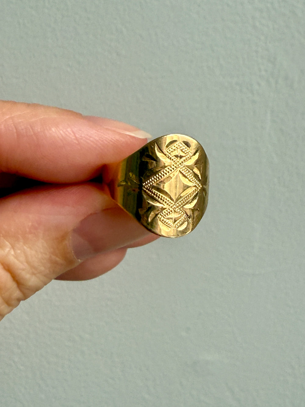 Gold ring with intricate design held by a hand against a light gray background