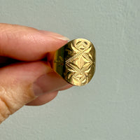 Gold ring with intricate design held by a hand against a light gray background