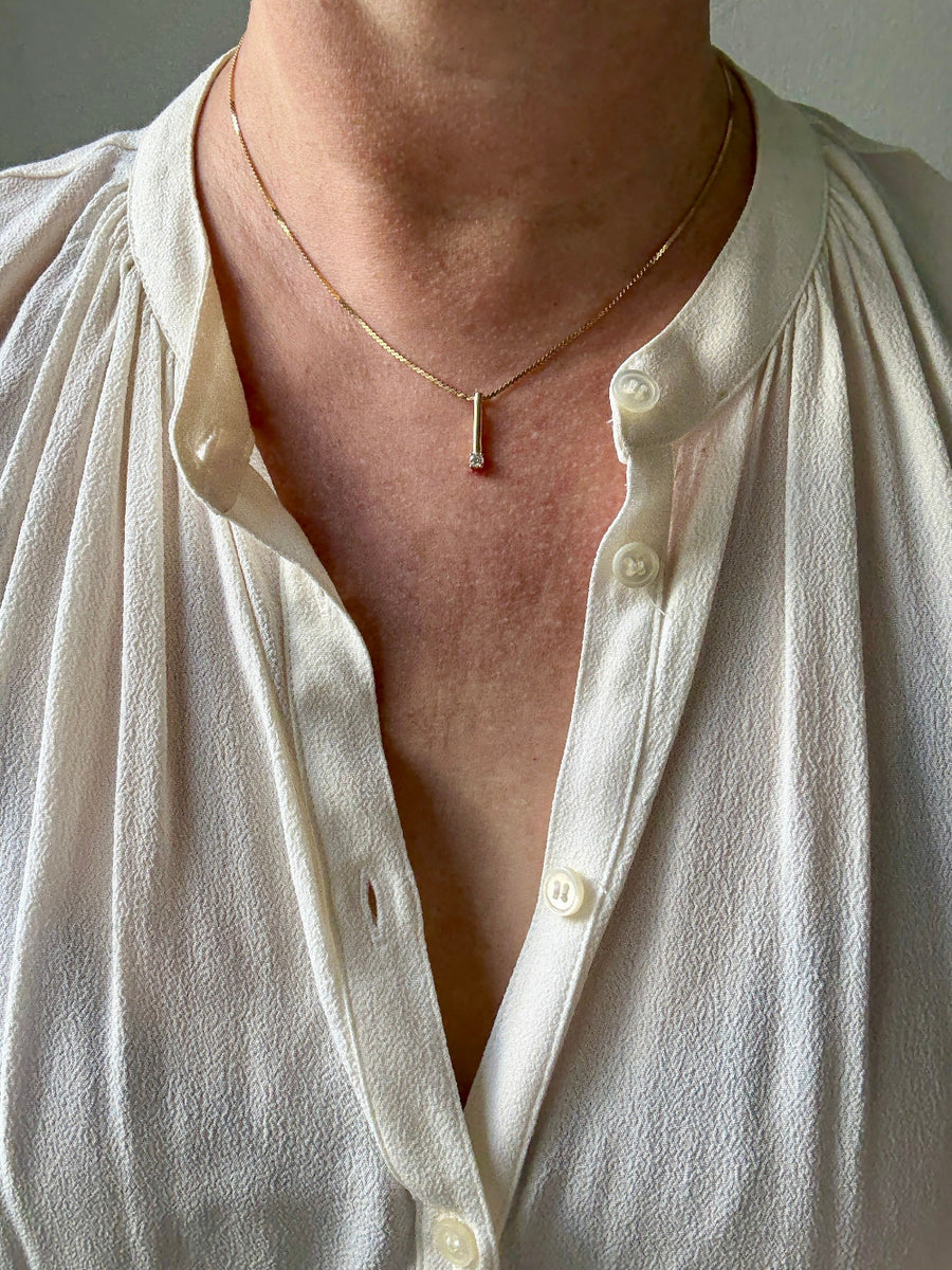 Person wearing a white shirt with buttons undone, revealing a necklace.