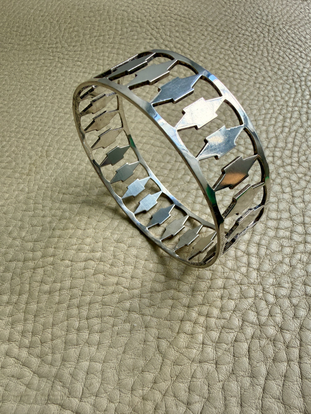 Silver bracelet with arrow design on a textured beige surface