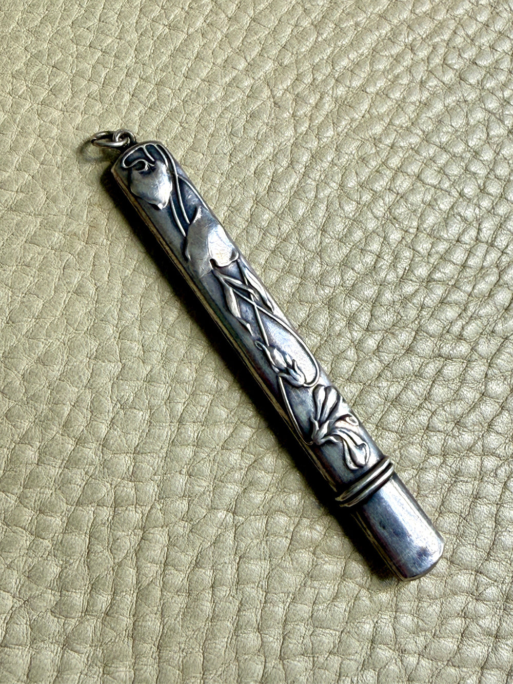Silver art nouveau pencil case with intricate designs on a textured beige surface