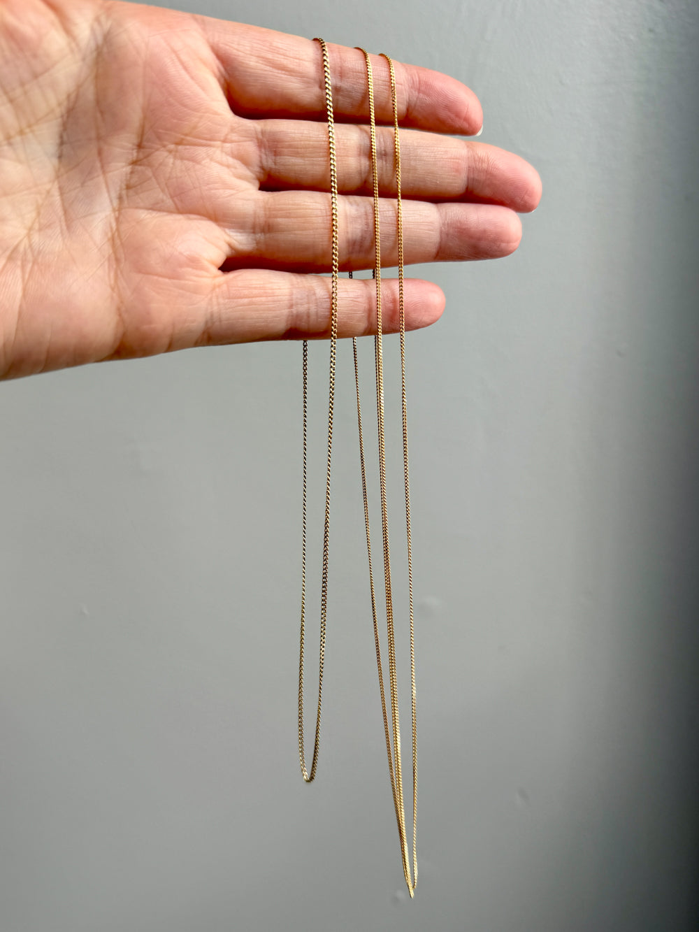 Gold curb necklaces of different lengths held by a hand against a gray background