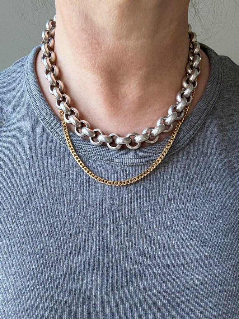 Two chain necklaces on a person wearing a gray shirt.