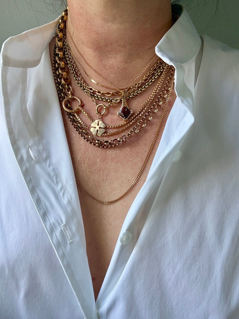 Person wearing multiple gold necklaces on a white shirt background