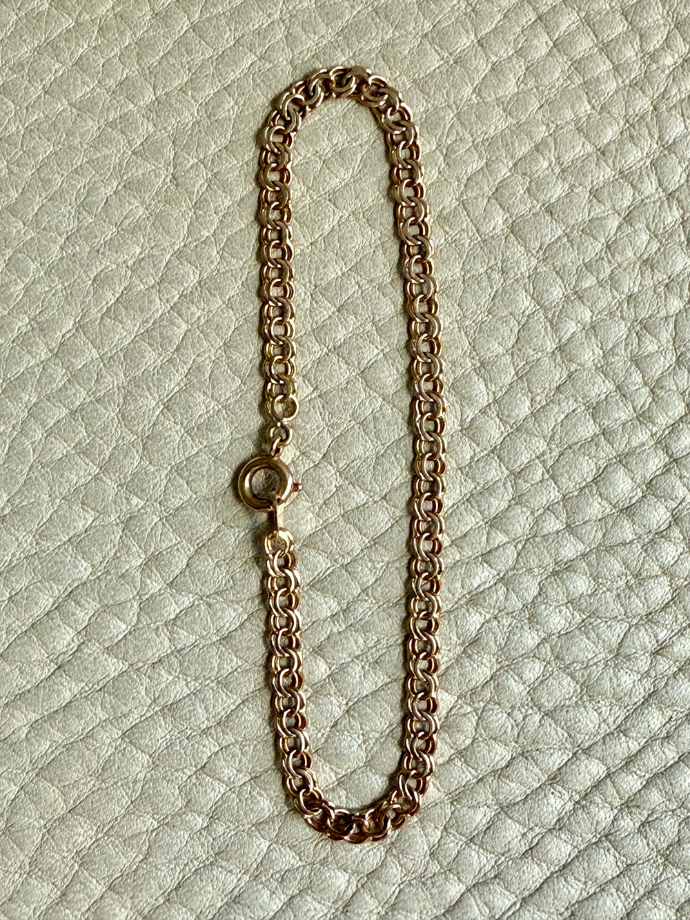 Gold chain bracelet on a textured light green background