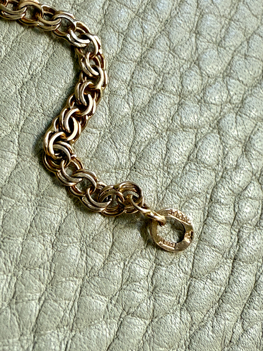 Gold chain bracelet on a textured light green surface