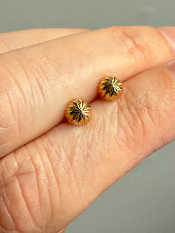 Gold earrings with star design held between two fingers against a neutral background
