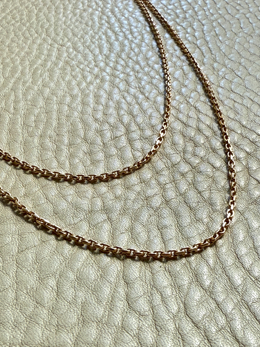 18k gold chains on a textured beige surface