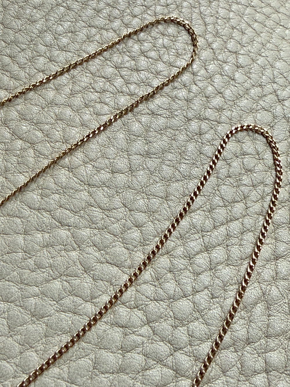 18k gold curb link necklace on a textured light gray surface