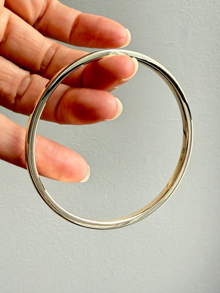 gold bangle held by a hand against a gray background