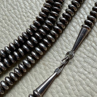 Silver beaded necklace with a clasp on a textured surface