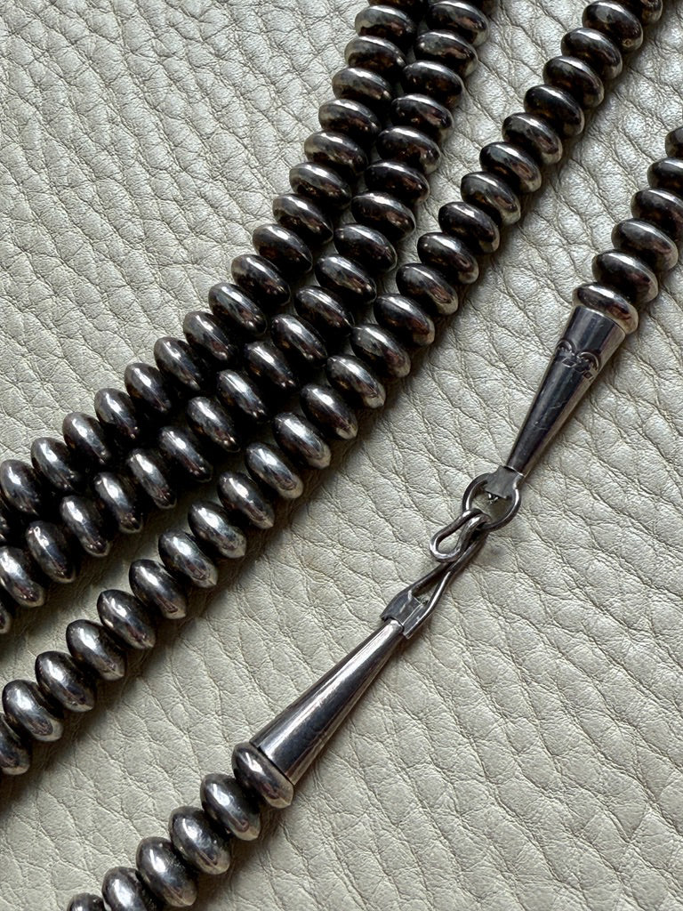 Silver beaded necklace with a clasp on a textured surface