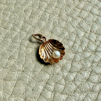vintage 14k Gold shell charm with a pearl on a textured beige background