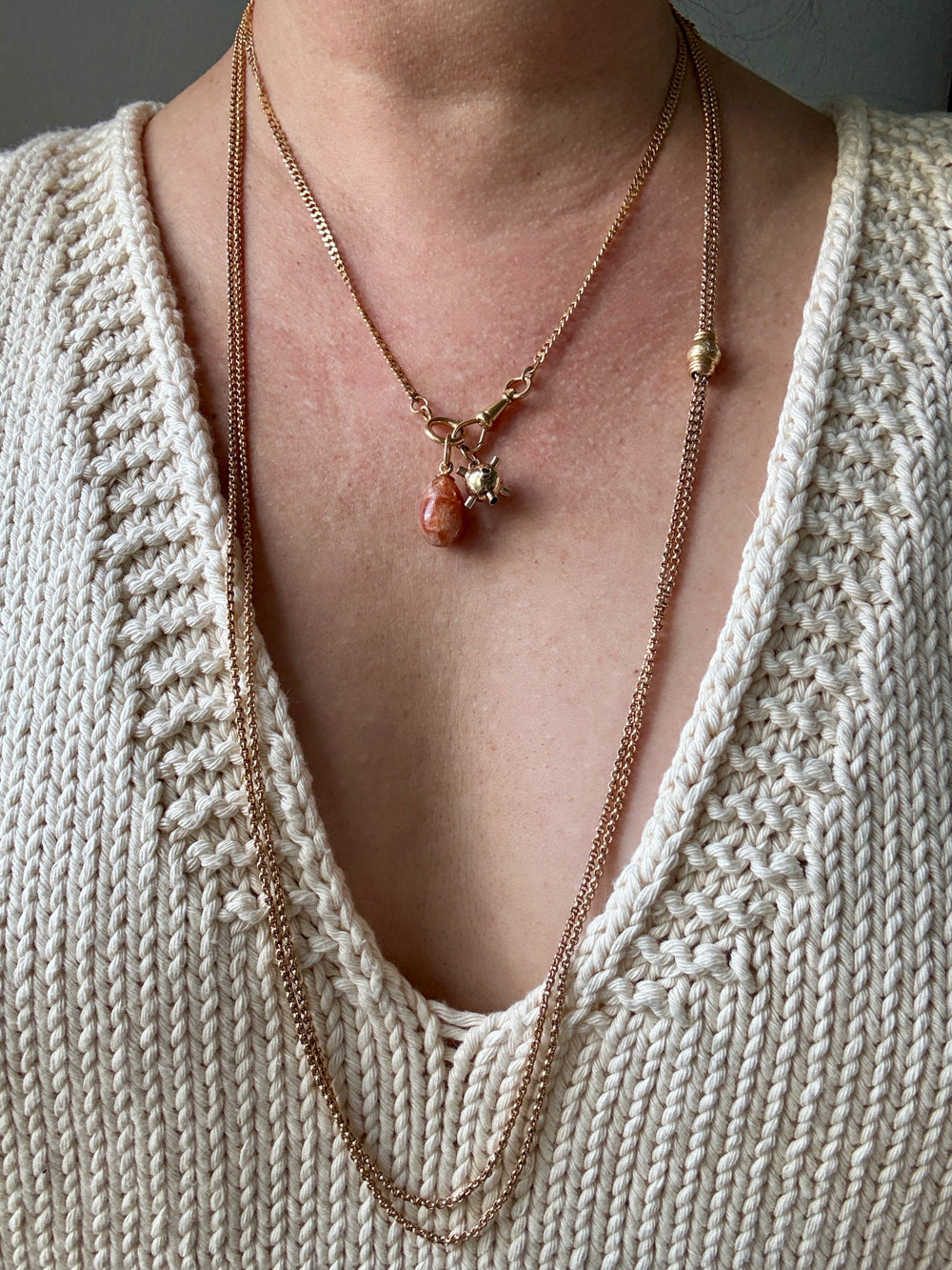 Necklaces with pendants on a person wearing a beige knit cardigan.