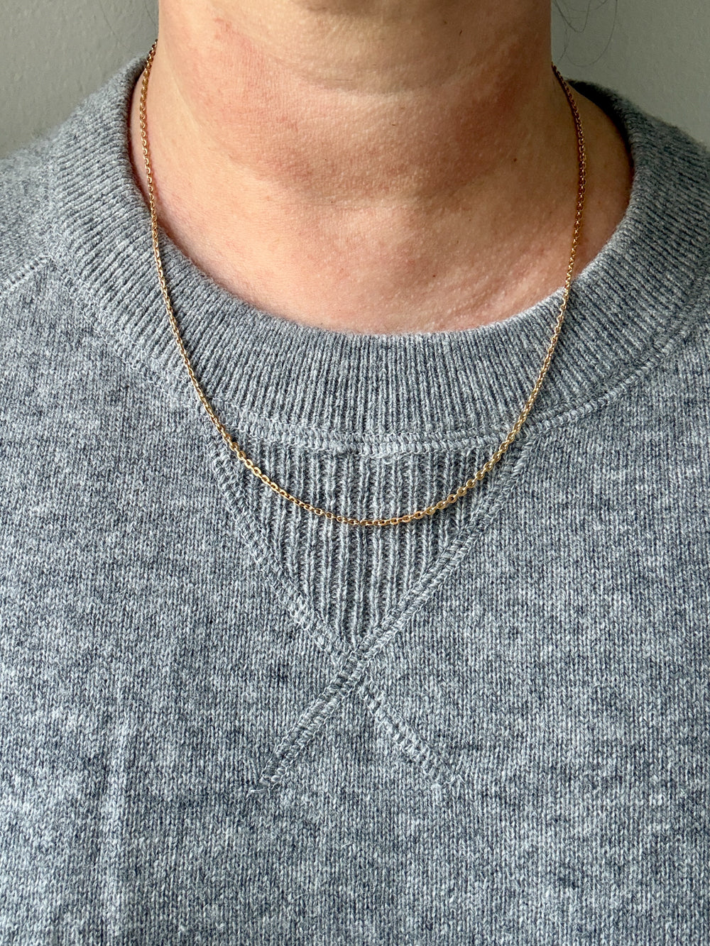 Person wearing a gold necklace with a plain background
