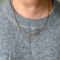 Person wearing a gold necklace with a plain background