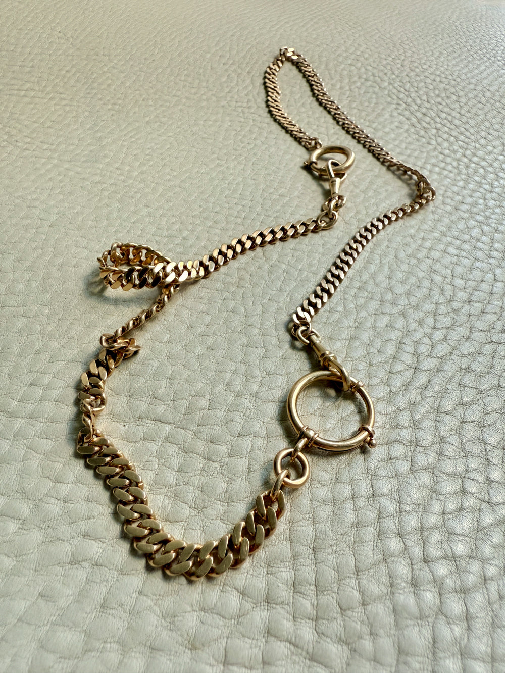 Gold watch chain necklace on a textured light gray surface. PenelopePenelope.com