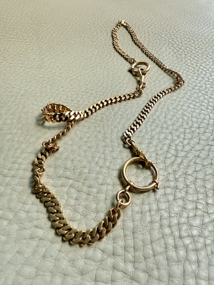 Gold watch chain necklace on a textured light gray surface. PenelopePenelope.com