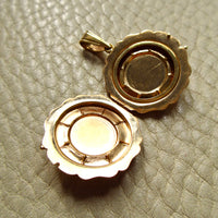 An open gold locket pendant with a scalloped edge, displayed on a textured light beige leather surface.
