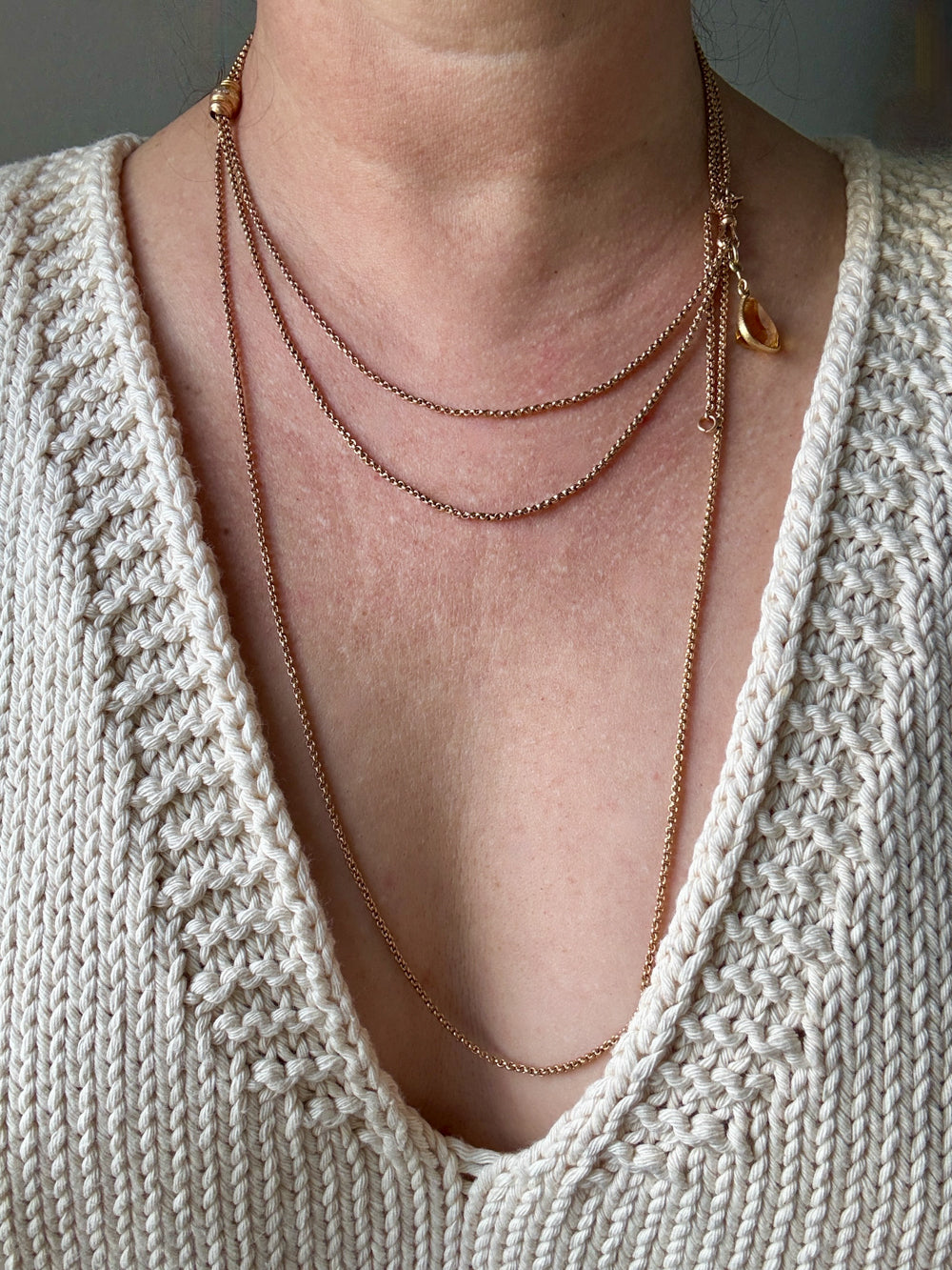 Close-up of a person wearing a delicate gold necklace with a textured beige sweater.