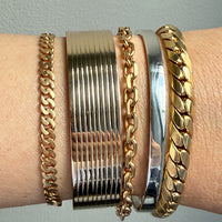 Gold bracelets on a wrist against a light gray background