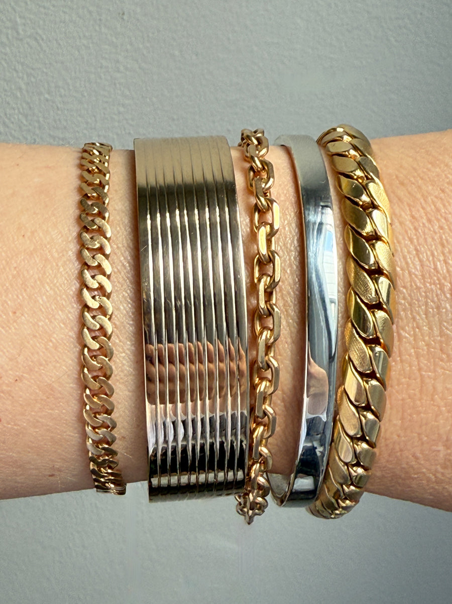 Gold bracelets on a wrist against a light gray background