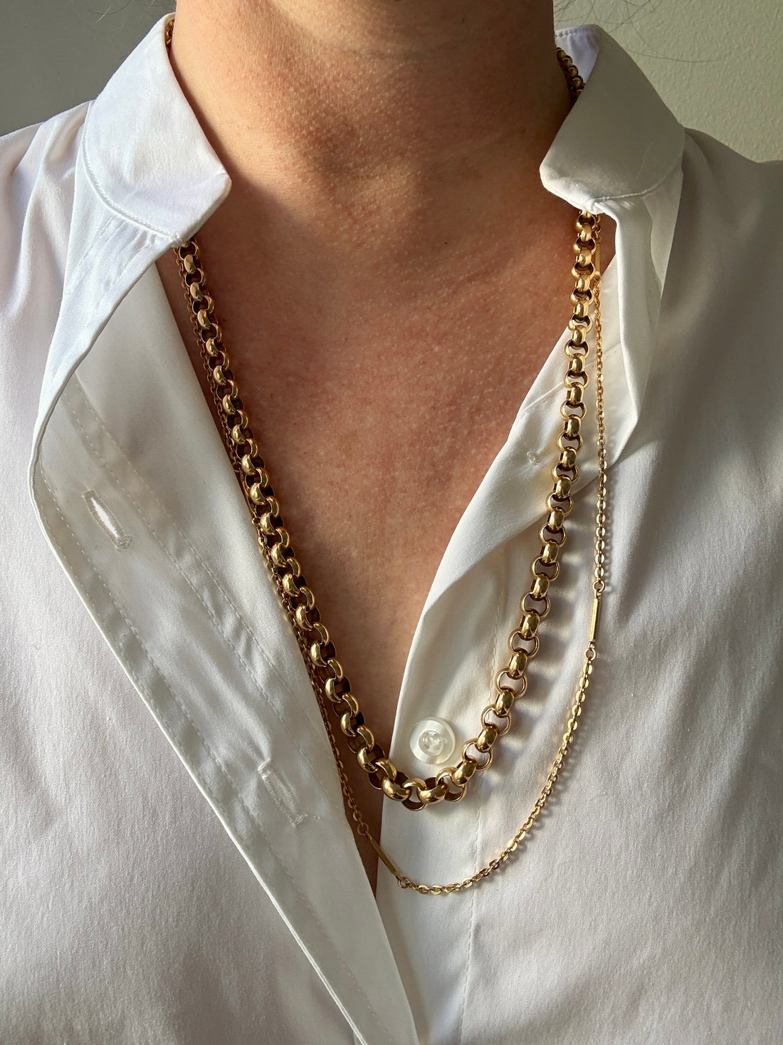 Gold chain necklaces worn by a person in a white shirt.