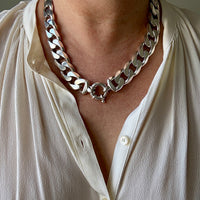Silver chain necklace worn by a person in a white shirt.