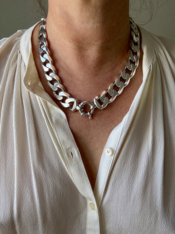 Silver chain necklace worn by a person in a white shirt.
