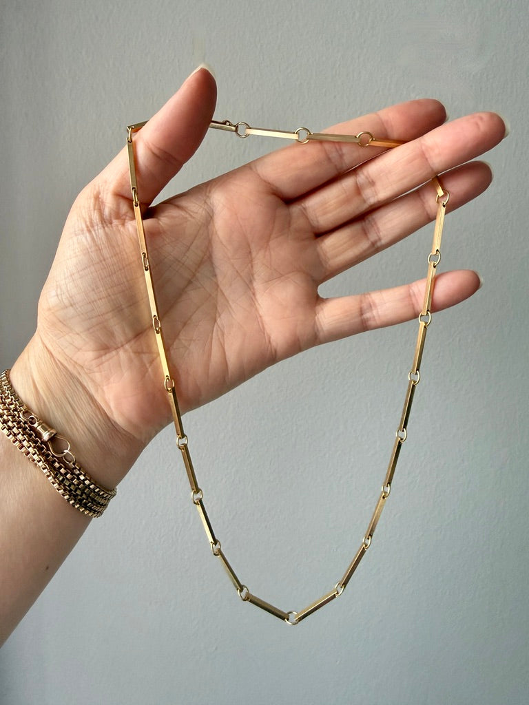 Gold necklace being held by a hand against a gray background