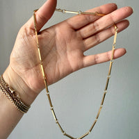 Gold necklace being held by a hand against a gray background