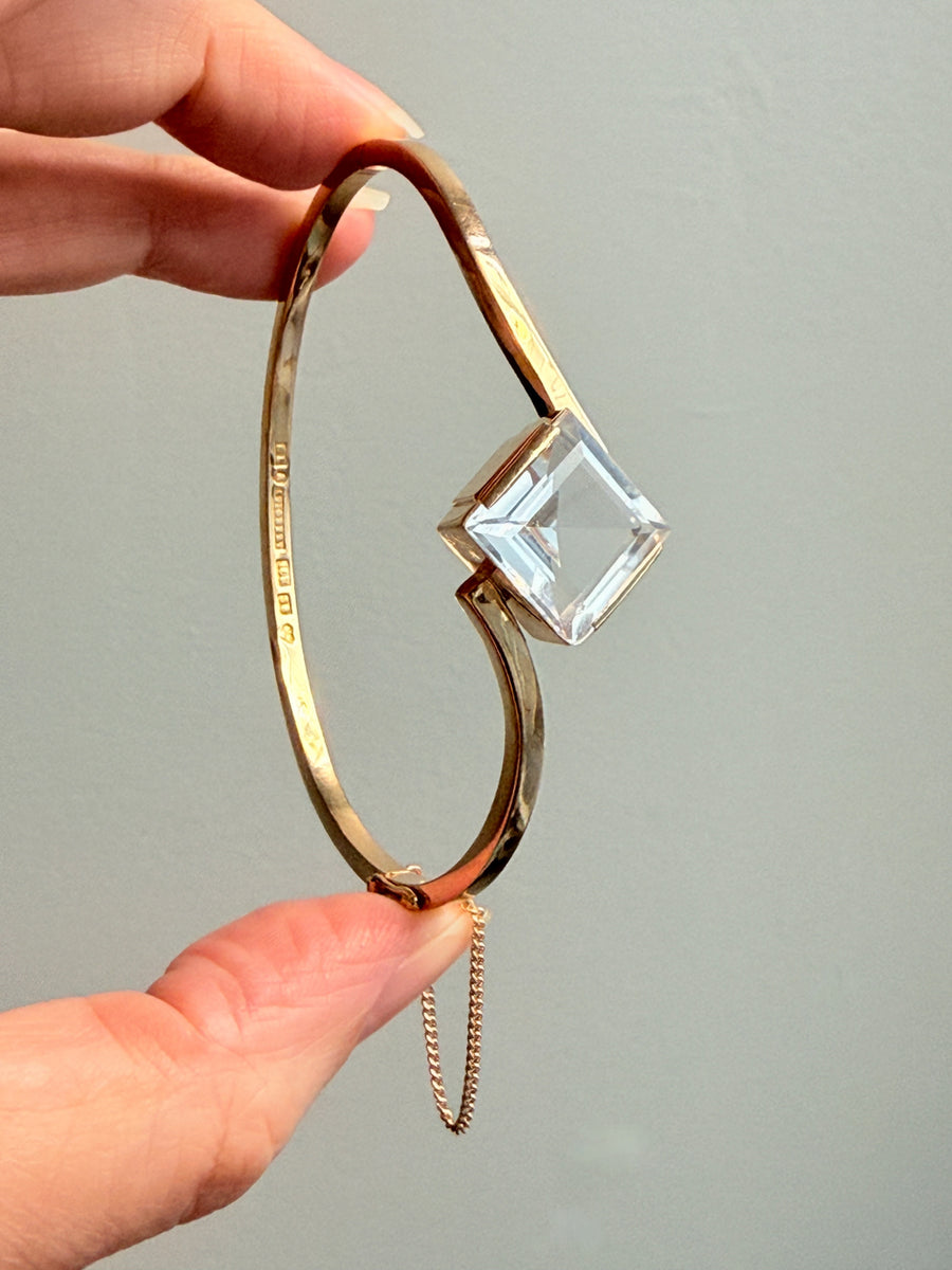 Gold bracelet with a clear crystal on a plain background. PenelopePenelope.com