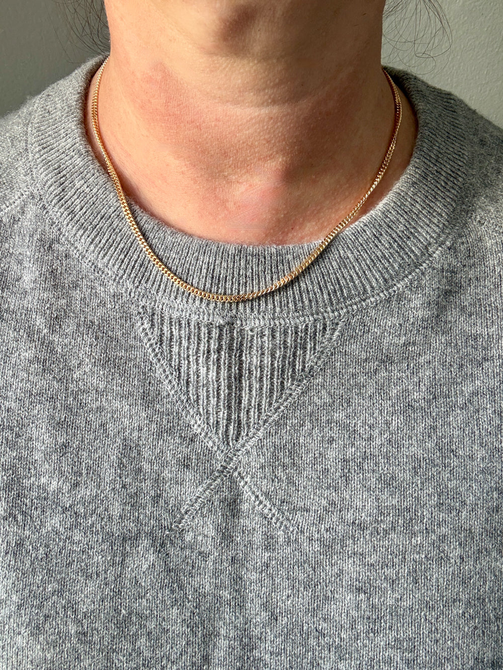Person wearing a gray sweater and gold necklace against a neutral background