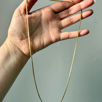 Hand holding a gold chain against a plain background