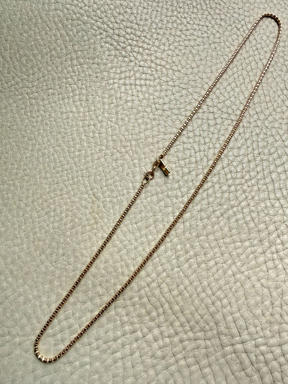 Gold chain necklace on a textured beige surface