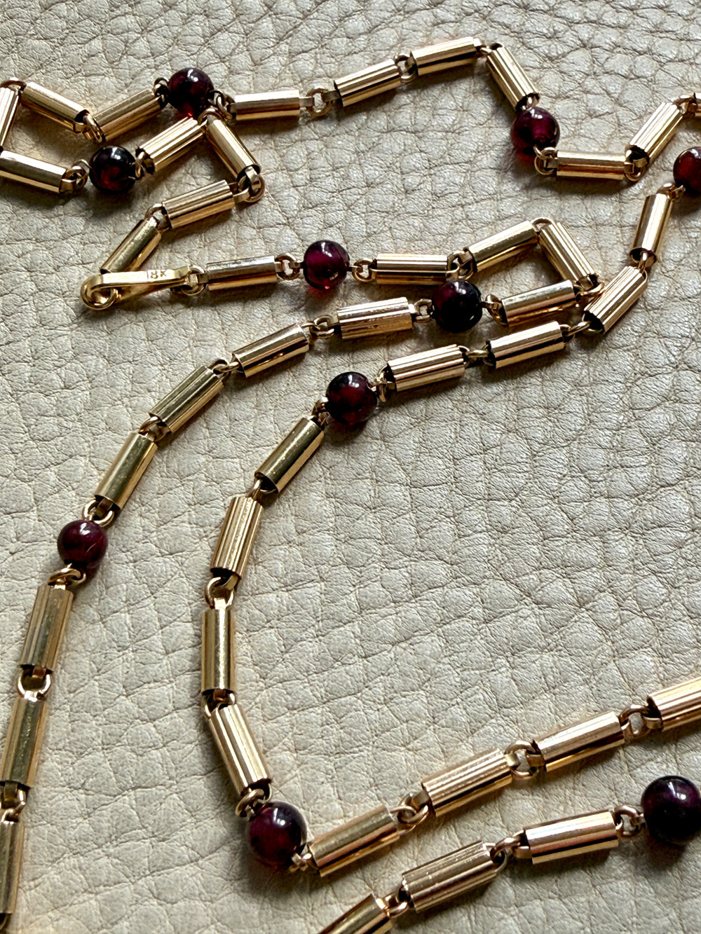 Gold necklace with garnet red beads on a textured surface