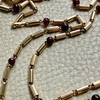 Gold necklace with garnet red beads on a textured surface