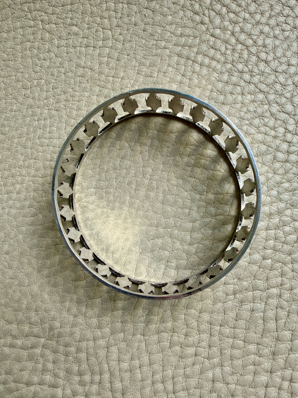 silver vintage bangle with decorative cutout on a textured beige surface