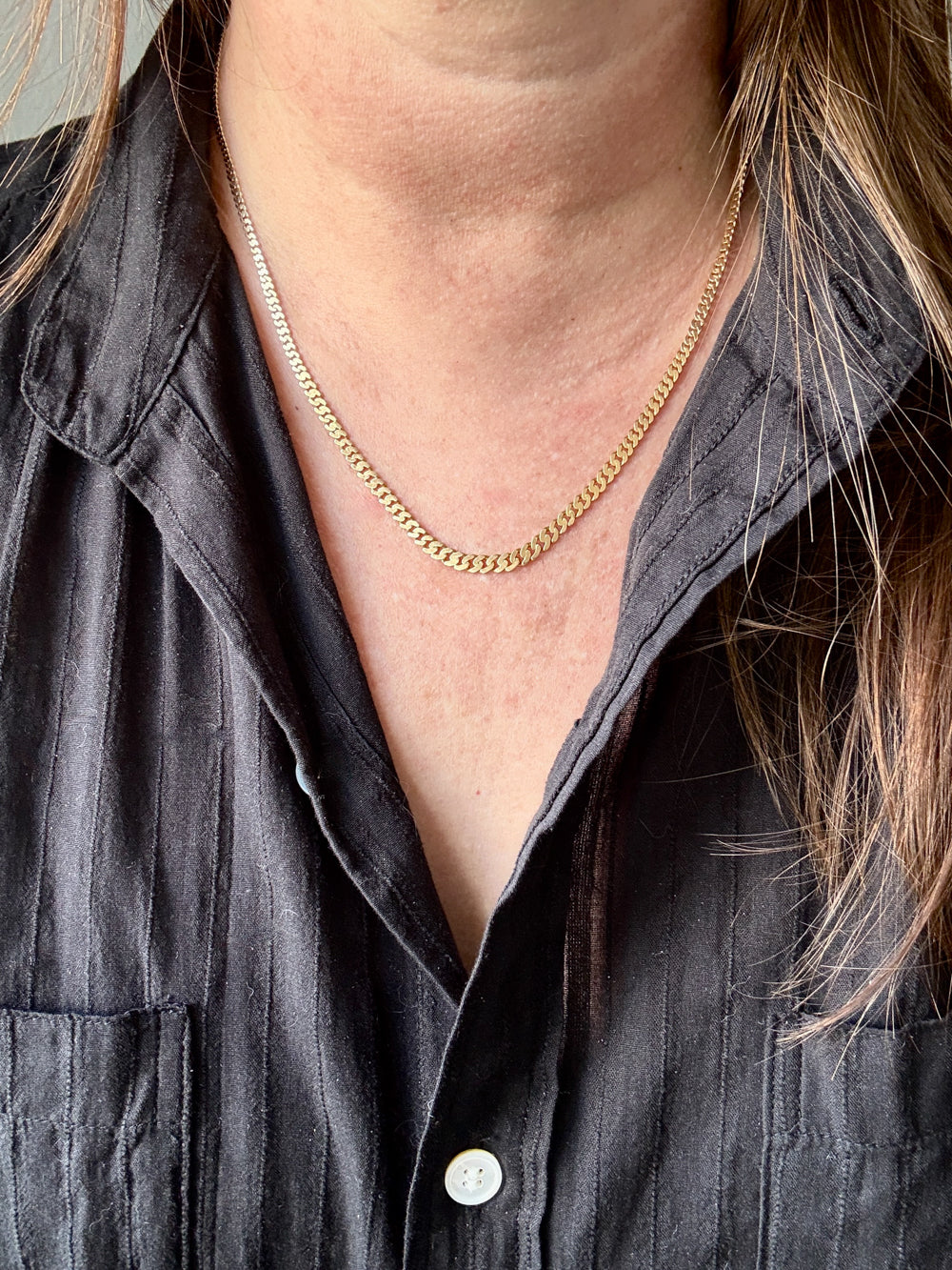 Person wearing a gold necklace with a gray shirt