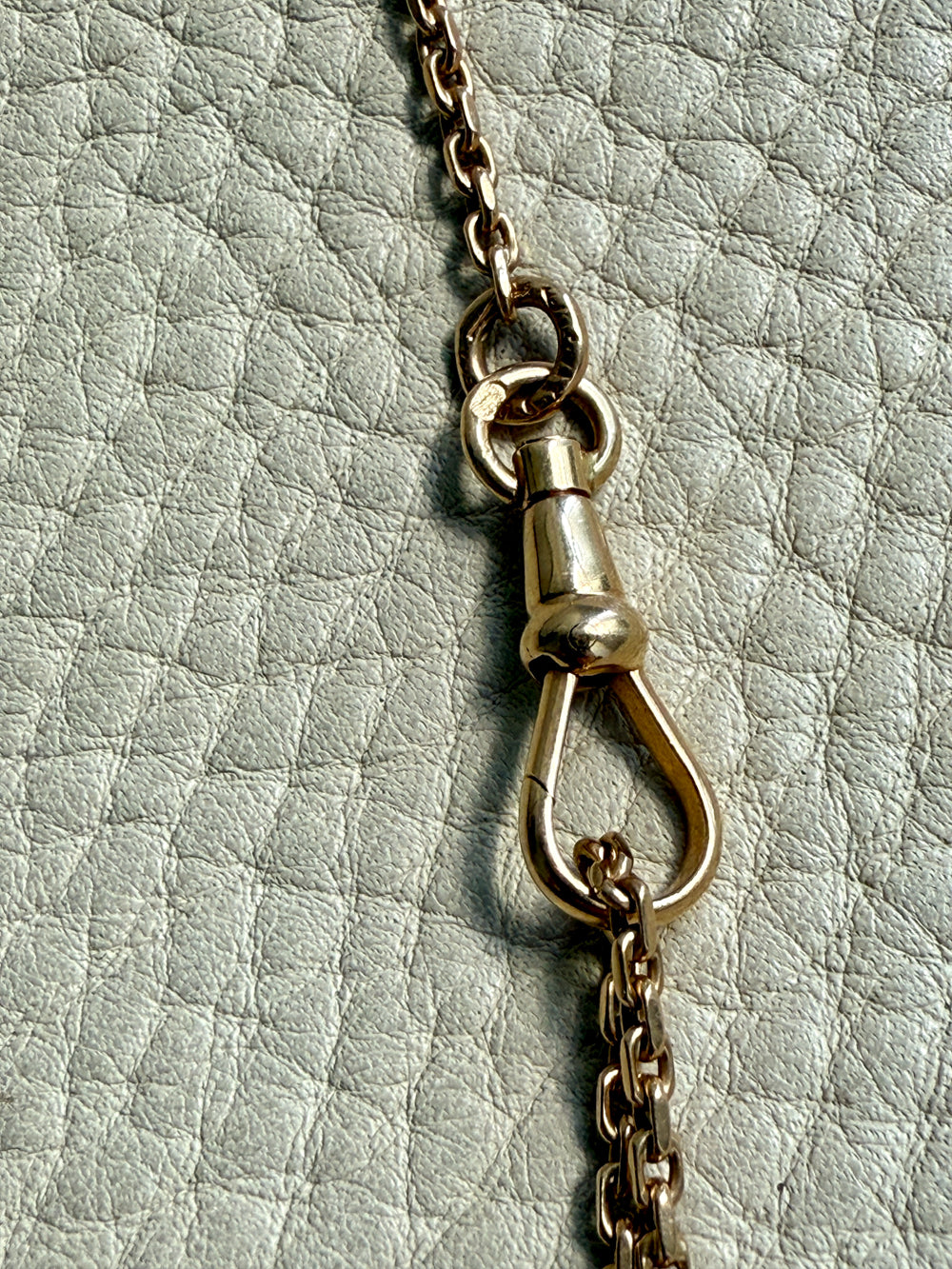 Close-up of a 18k gold chain with a swivel dog clip clasp on a textured light gray background