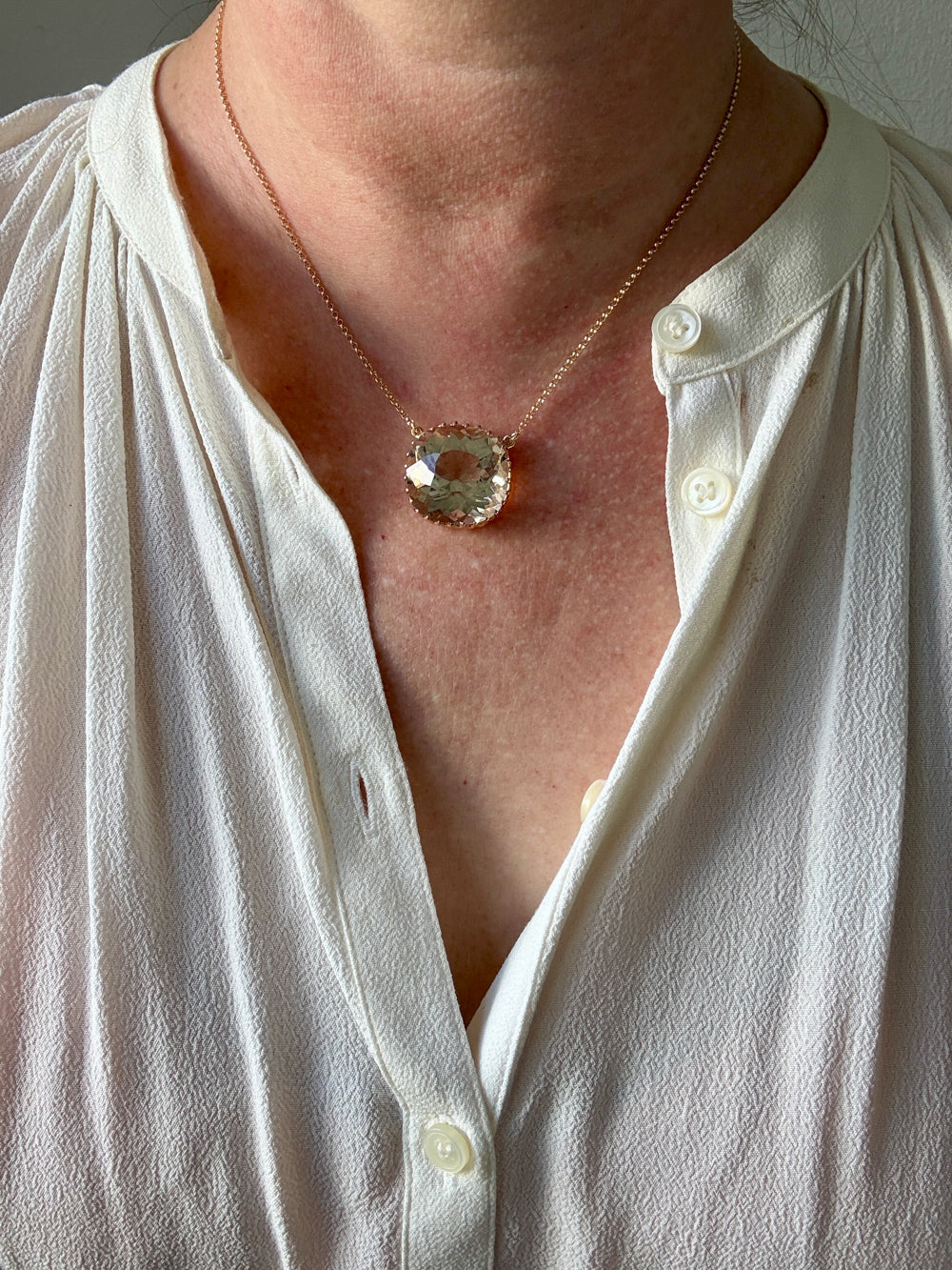 Necklace with a large pendant worn by a person in a white shirt.