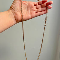 Gold chain held in a hand against a neutral background